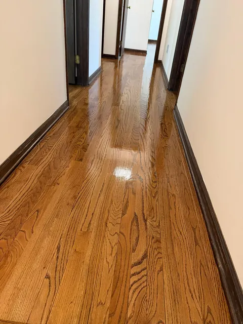 After: the same hallway sanded and refinished, glossy oak with dark trim