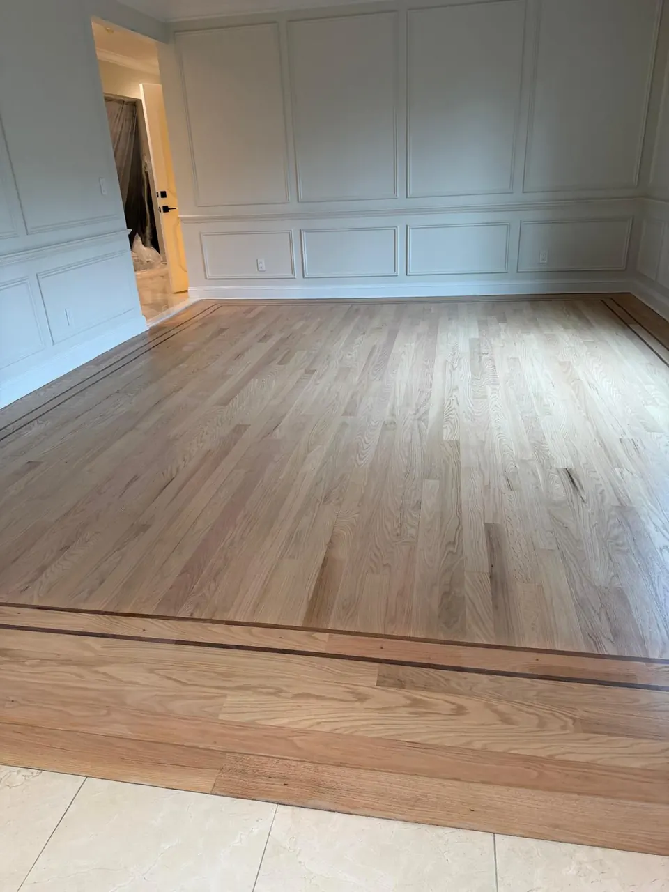 New white oak plank floor installed in a large room with wainscoting