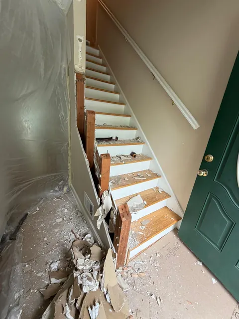 Before: staircase with damaged treads and demolition debris next to a green front door
