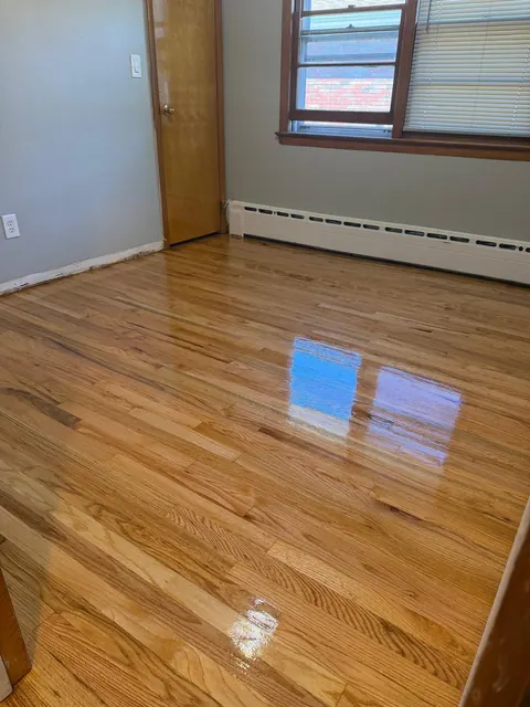 Glossy refinished oak floor under a window with baseboard heat
