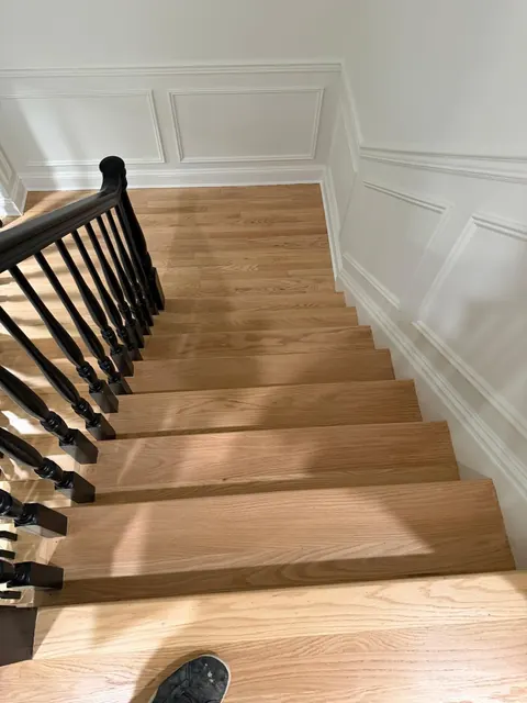 Natural oak stairs with black iron balusters and white wainscoting