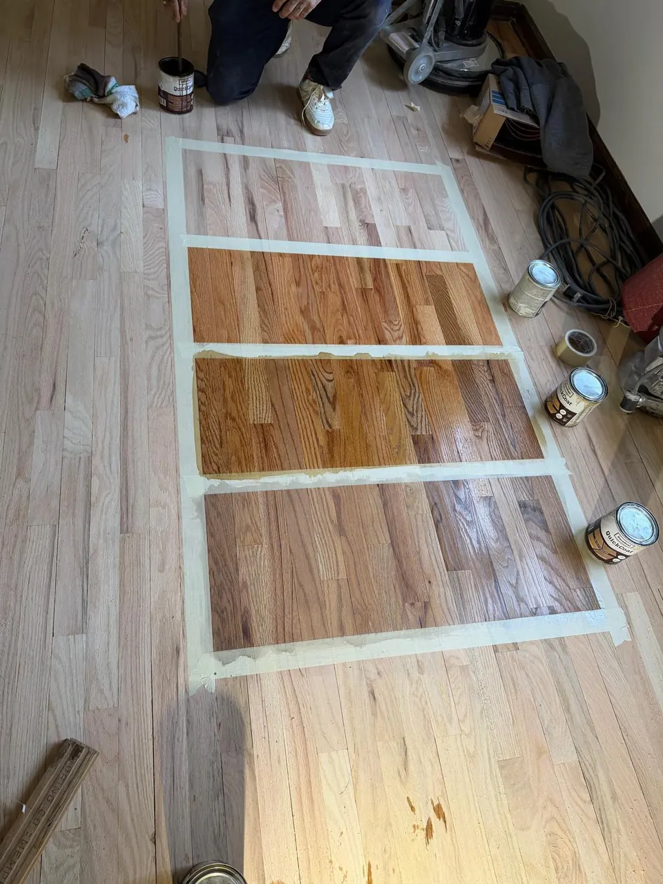 Six stain samples on an oak floor with cans of stain beside them